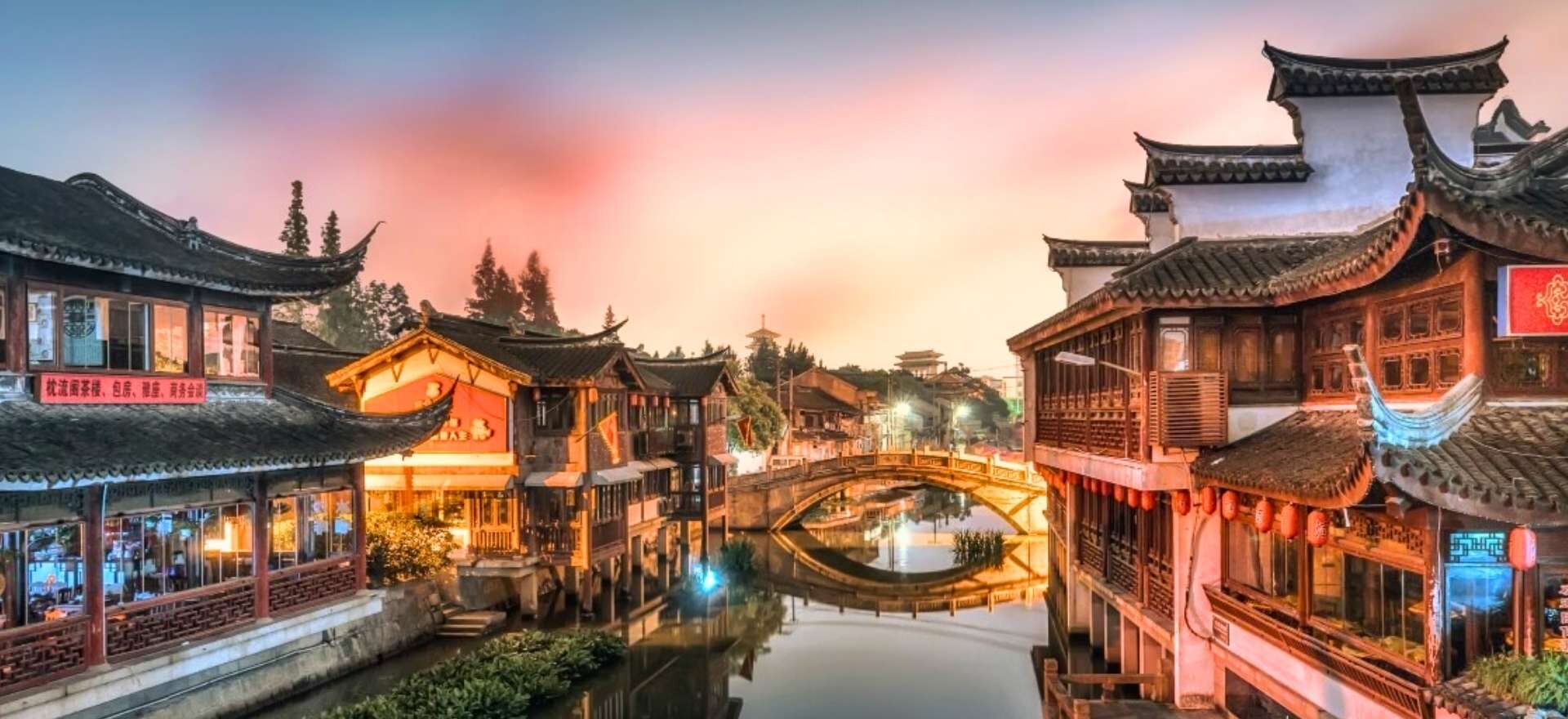 Casas tradicionales iluminadas y puente de piedra sobre el agua en la etapa de Shanghái, dentro del circuito China con Panda de Traveland.