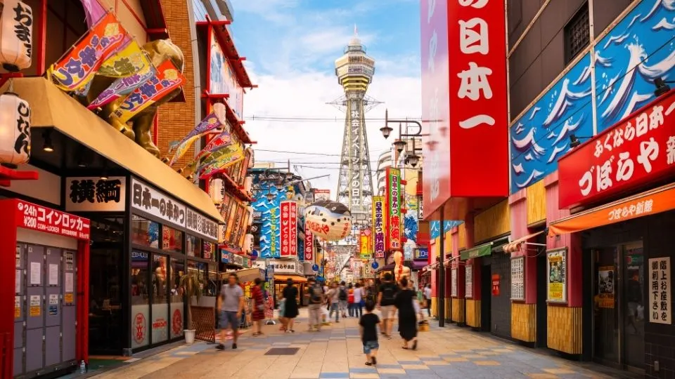 Calle peatonal llena de letreros en el barrio de Shinsekai con la torre Tsutenkaku al fondo en Osaka Japón con Traveland
