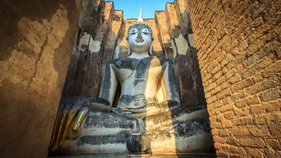 Gran estatua de Buda Phra Atchana sentado entre muros de piedra en el templo Wat Si Chum Sukhothai Tailandia con Traveland