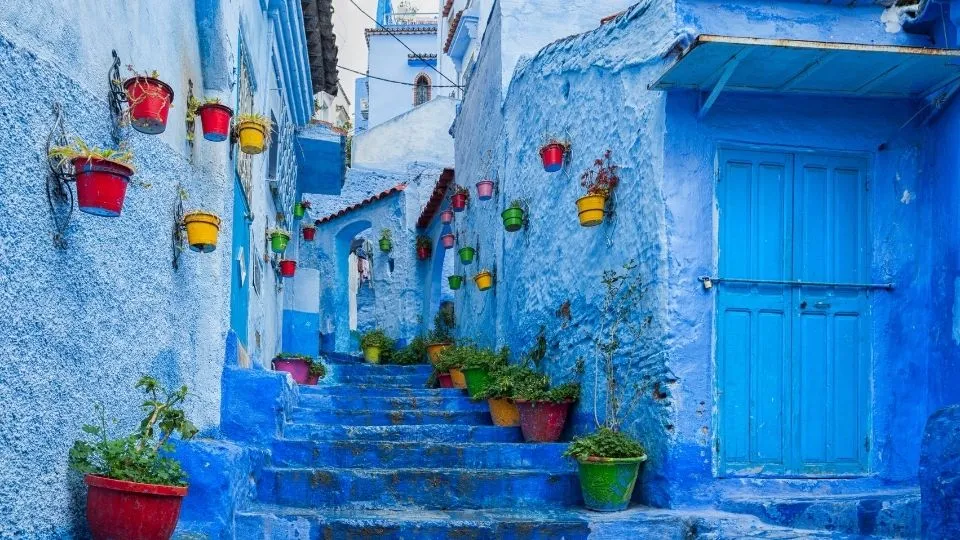 Callejon escalonado azul con macetas de colores en las paredes de la medina de Chefchaouen Marruecos con Traveland