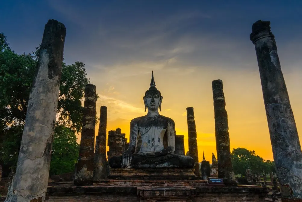 Estatua de Buda sentado entre columnas en las ruinas de Wat Mahathat al atardecer en Sukhothai Tailandia al Completo con Traveland