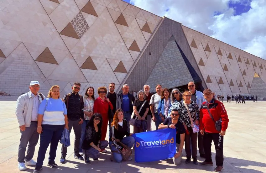 Grupo de viajeros con la pancarta de Traveland frente a la fachada arquitectonica del Gran Museo Egipcio en El Cairo Guiza