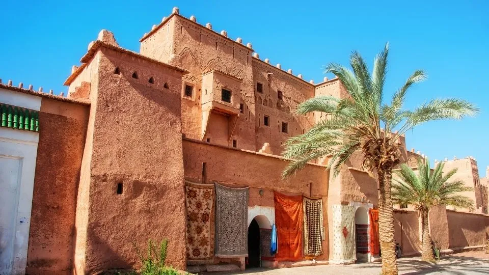Fachada de adobe de la Kasbah Taourirt con alfombras tradicionales y palmeras en Ouarzazate Marruecos con Traveland