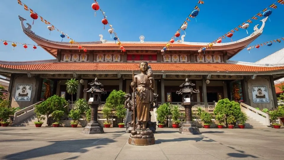 Estatua de Buda de pie y fachada de la pagoda Vinh Nghiem decorada con farolillos en Ho Chi Minh Vietnam con Traveland