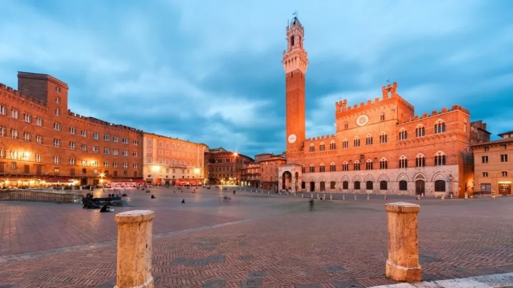 Vista de la Plaza del Campo iluminada con el Palazzo Pubblico y la Torre del Mangia en Siena Italia con Traveland