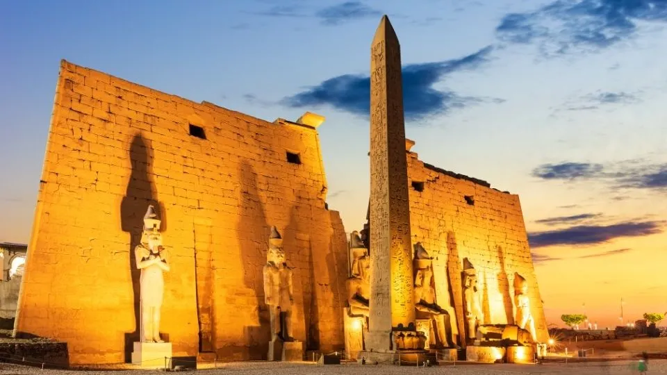 Fachada iluminada del Templo de Luxor al anochecer con el obelisco de Ramses II y estatuas colosales en Egipto con Traveland